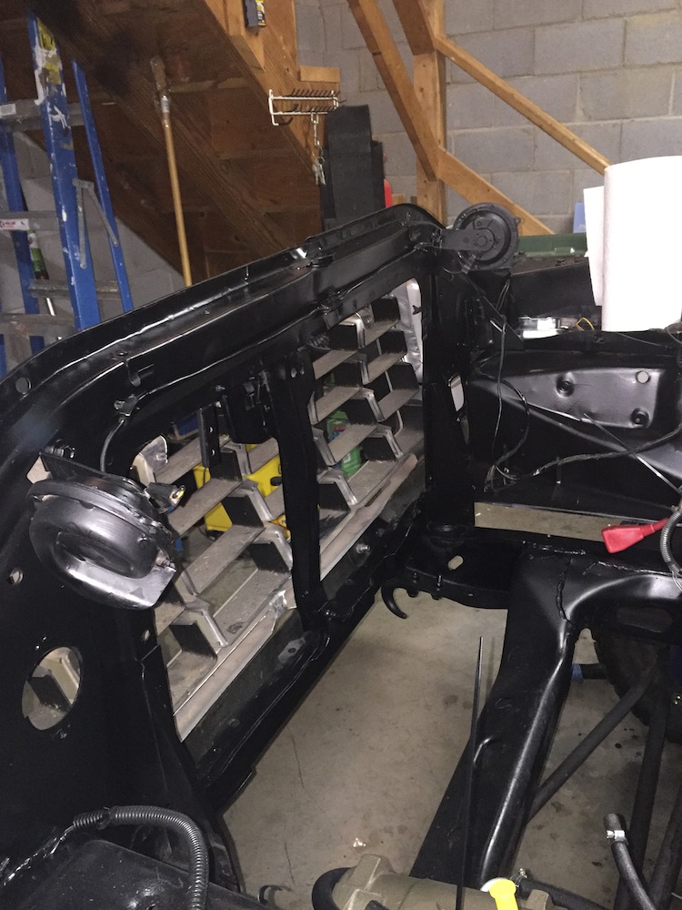 Black painted vehicle frame, front grille area, and suspension parts in a garage.