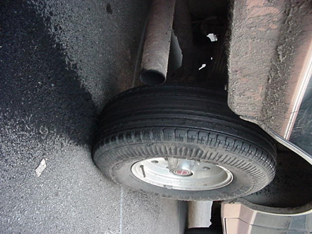 Sideways close-up of a tire on a silver steel wheel with exhaust pipe visible, parked on asphalt