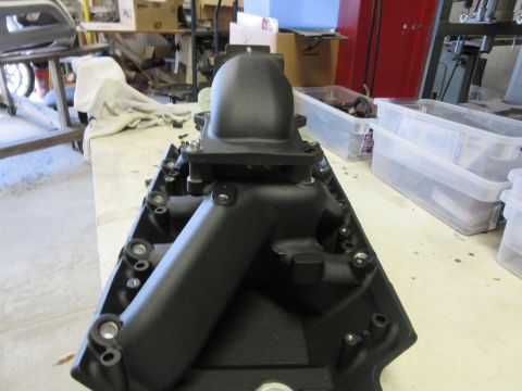 Black aftermarket intake manifold on a workbench with storage bins in the background.
