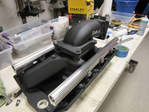Black Edelbrock intake manifold with polished fuel rails on a workbench.