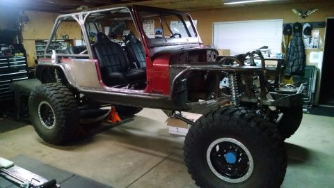 1985 Jeep CJ7 - A custom-built Jeep CJ7 is shown in a garage, featuring a roll cage, large off-road tires, and a red body with exposed metal panels. The ve…