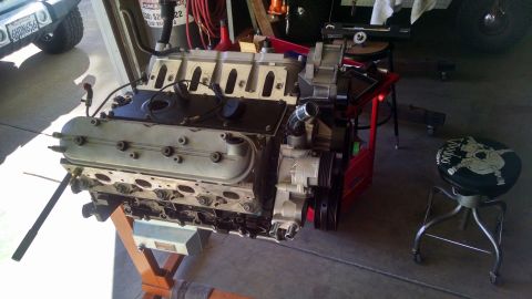 1985 Jeep CJ7 - A V8 engine with a supercharger is mounted on an orange engine stand in a garage. A Jeep CJ7 is partially visible in the background.
