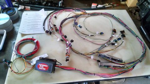 1985 Jeep CJ7 - A complex automotive wiring harness is laid out on a white surface, featuring numerous connectors, color-coded wires, and a central control…