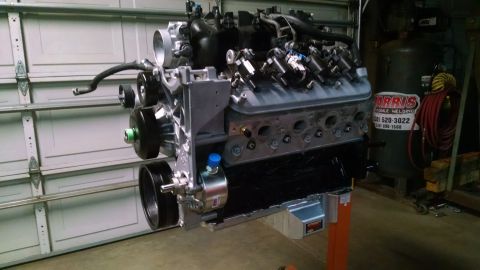 1985 Jeep CJ7 - A rebuilt V8 engine is mounted on an orange engine stand in a garage, in front of a closed garage door. The engine has a black oil pan and…