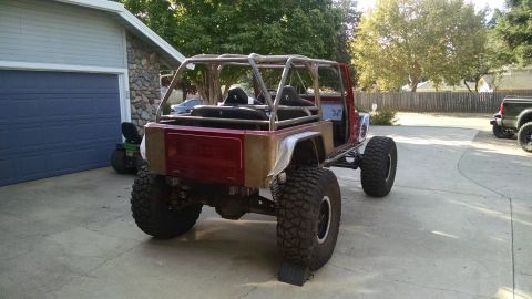 1985 Jeep CJ7 - The rear driver's side of a custom-built, red Jeep CJ7 is shown parked on a concrete driveway in front of a garage. The vehicle features a…