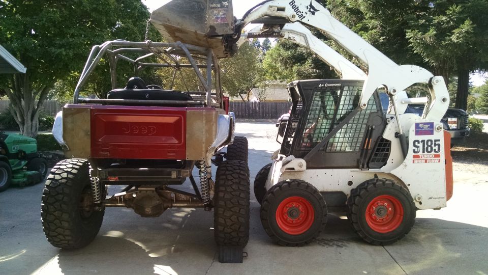 Modified red Jeep CJ7 next to a white Bobcat S185 skid steer loader.