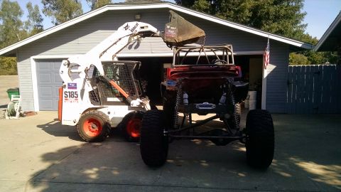 1985 Jeep CJ7 - A white Bobcat S185 skid steer loader is lifting a bucket over the rear of a red Jeep CJ7 with a roll cage. The vehicles are parked in fron…