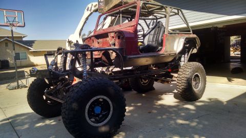 1985 Jeep CJ7 - A custom-built, red Jeep CJ7 is shown from a 3/4 front angle, lifted with large off-road tires and a roll cage. The vehicle is parked on a…