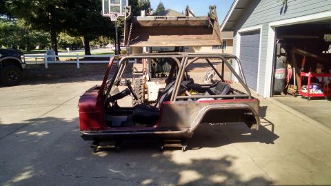1985 Jeep CJ7 - A partially disassembled red Jeep CJ7 is parked on a concrete driveway in front of a garage. A front-end loader is positioned above the Jee…