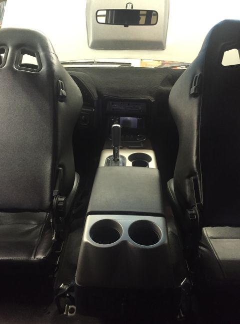1988 Ford Bronco - The interior of a vehicle shows two black racing seats facing forward, with a center console featuring cup holders and a gear shifter. A da…
