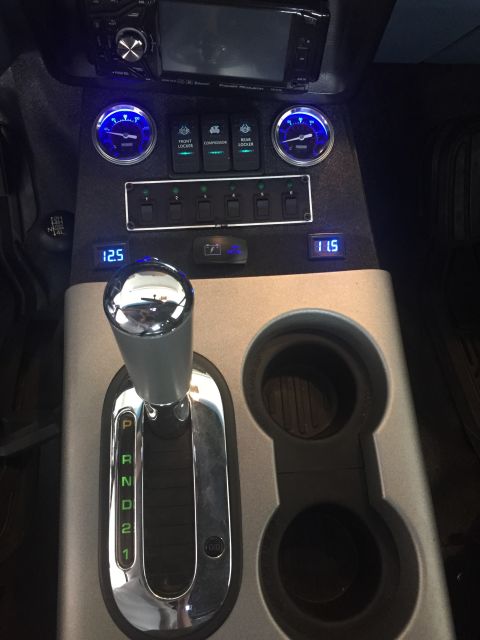 1988 Ford Bronco - The interior of a vehicle shows a modified center console with multiple switches, gauges, and a digital display. A chrome automatic gear sh…