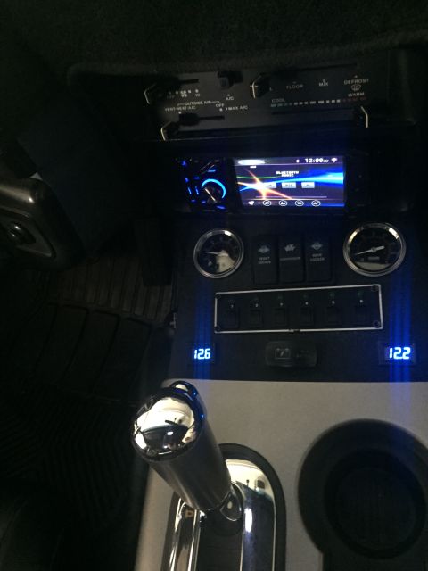 1988 Ford Bronco - The interior of a vehicle shows a modified dashboard with an aftermarket stereo, climate controls, and several toggle switches. A chrome-pl…