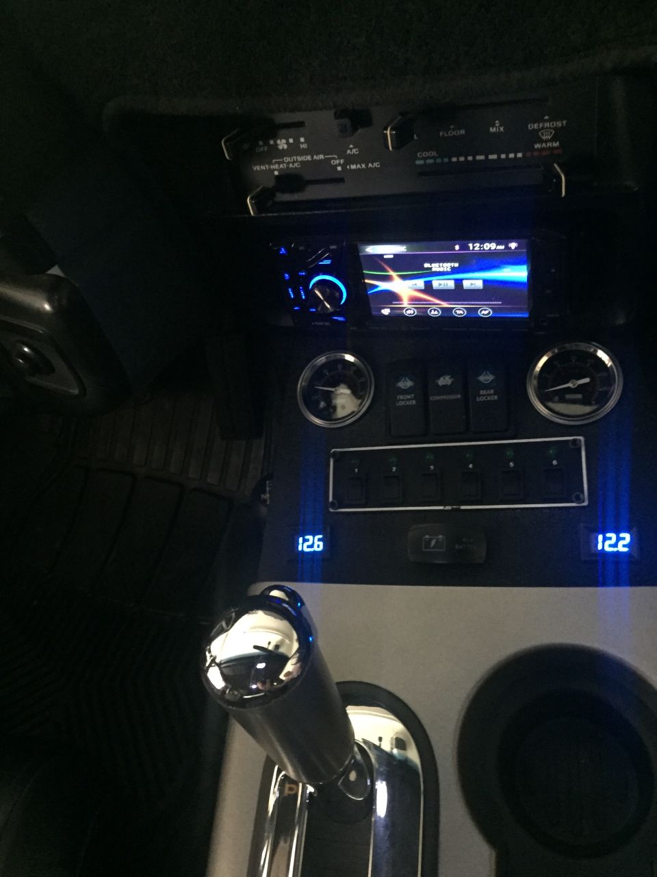 Vehicle interior showing aftermarket stereo, climate controls, toggle switches, and gear shifter.