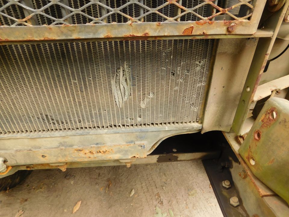 Close-up of dented radiator and mesh grille on a rusty olive-green military vehicle