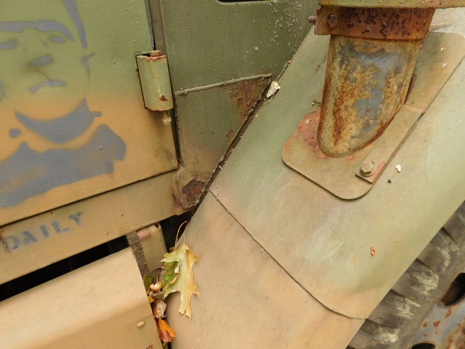 Weathered olive-drab vehicle body with rust, stencil art, and text.