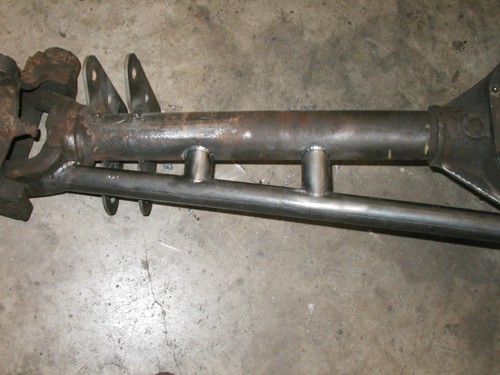 Bare solid front axle housing with spring perches and tie rod on a shop floor