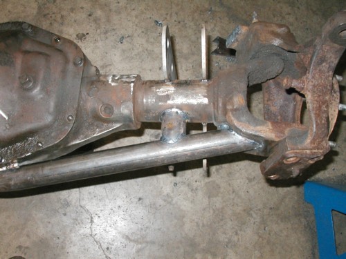 Bare front axle housing with differential, knuckle and fresh weld beads on a shop floor