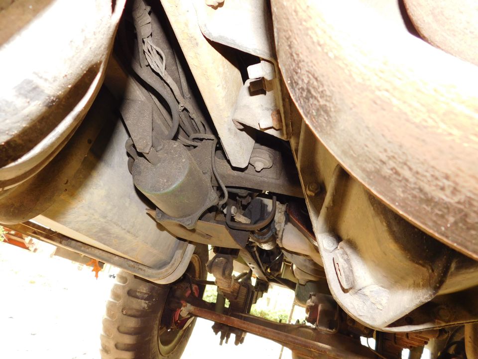 Underside of a vehicle showing suspension, exhaust, fuel tank, and tire.