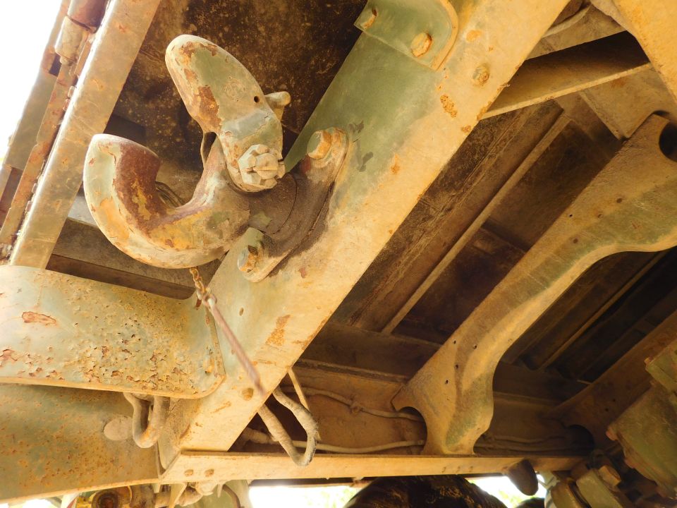 Underside of a vehicle showing a rusted tow hook assembly on a green metal frame.