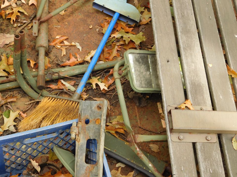 Outdoor scene with broom, blue crate, metal bench parts, and fallen leaves.