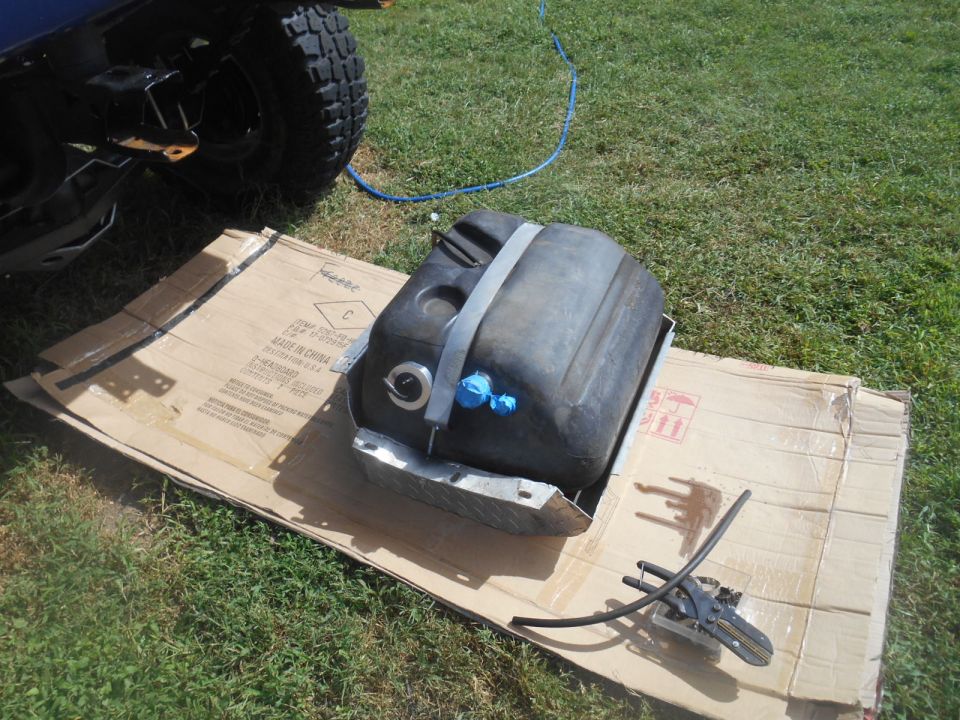 Black plastic fuel tank on cardboard with vehicle tire in background