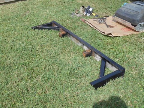 1972 Ford Bronco - A black metal trailer hitch frame is laid out on a grassy lawn. Tools and a black plastic fuel tank are visible in the background on a piec…