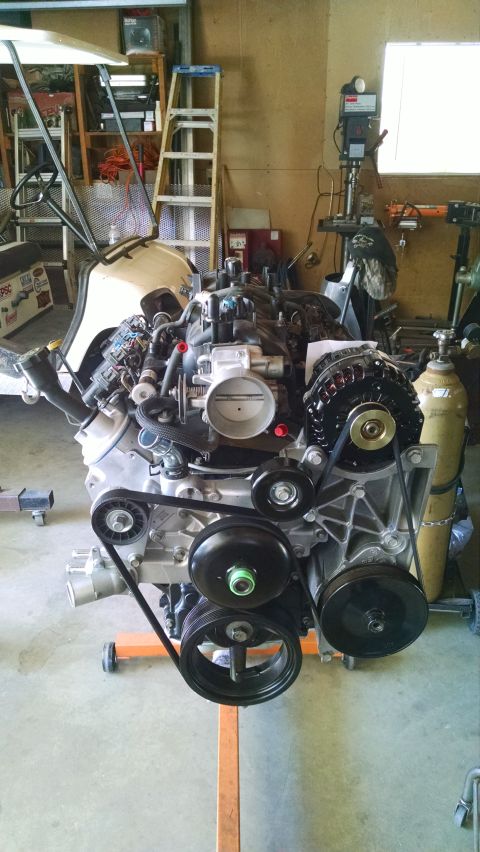 1985 Jeep CJ7 - A V8 engine assembly is mounted on an orange engine stand in a garage. The engine features a black alternator, multiple pulleys, and a thro…
