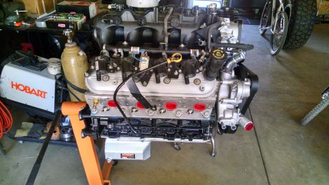 1985 Jeep CJ7 - A V8 engine is mounted on an orange engine stand in a garage setting. A Hobart welder and a gas cylinder are visible to the left of the eng…