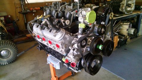 1985 Jeep CJ7 - A close-up, angled view of a V8 engine with a supercharger mounted on an orange engine stand. The engine features a black serpentine belt s…