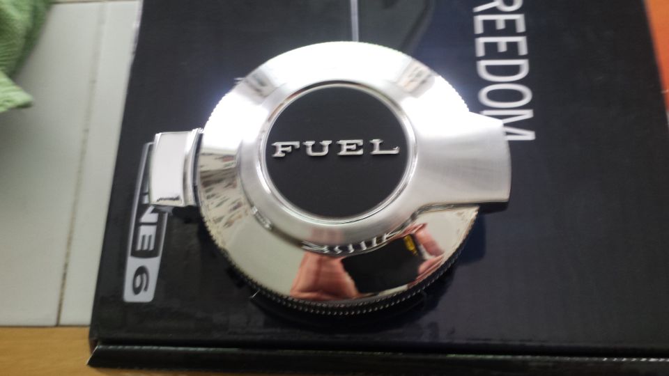 Chrome fuel door with "FUEL" text on a black background, resting on a book.