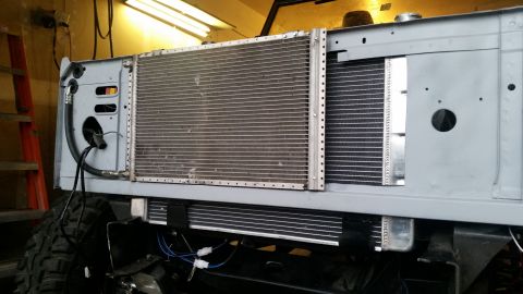 1979 Ford Bronco - The front end of a vehicle is shown with a large radiator and a smaller condenser installed. Hoses and electrical wires are visible connect…