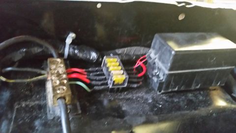 1979 Ford Bronco - A close-up view of a vehicle's electrical wiring, including a brass terminal block, a clear fuse holder with yellow fuses, and a black plas…