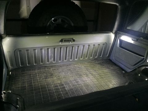 1988 Ford Bronco - The interior cargo area of a vehicle, likely an SUV, features a rubber floor mat and a ribbed panel on the rear wall. A spare tire is visib…