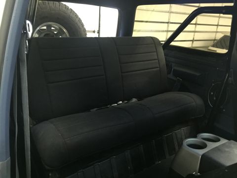 1988 Ford Bronco - The interior of a dark blue vehicle shows a black bench seat with horizontal stitching. A spare tire is visible through the rear window.