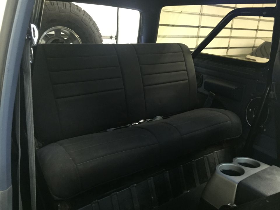 Interior of a dark blue vehicle showing a black bench seat and a spare tire in the back.