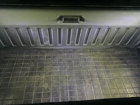 1988 Ford Bronco - Inside a pickup bed showing ribbed tailgate, recessed handle, and a square-pattern rubber bed mat on the floor.