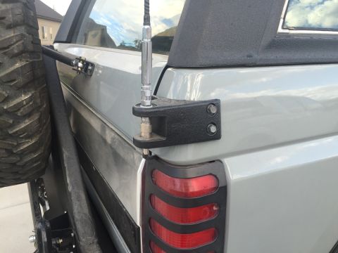 1988 Ford Bronco - A close-up rear-side view of a light gray SUV shows a mounted CB antenna and a spare tire carrier with a spare tire attached.