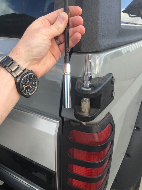 1988 Ford Bronco - A person's hand holds a black antenna with a chrome base, preparing to attach it to a black mounting bracket on the rear corner of a light…