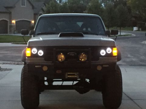 1988 Ford Bronco - Front view of a modified gray 1987 Ford Bronco with aftermarket lights and bumper.