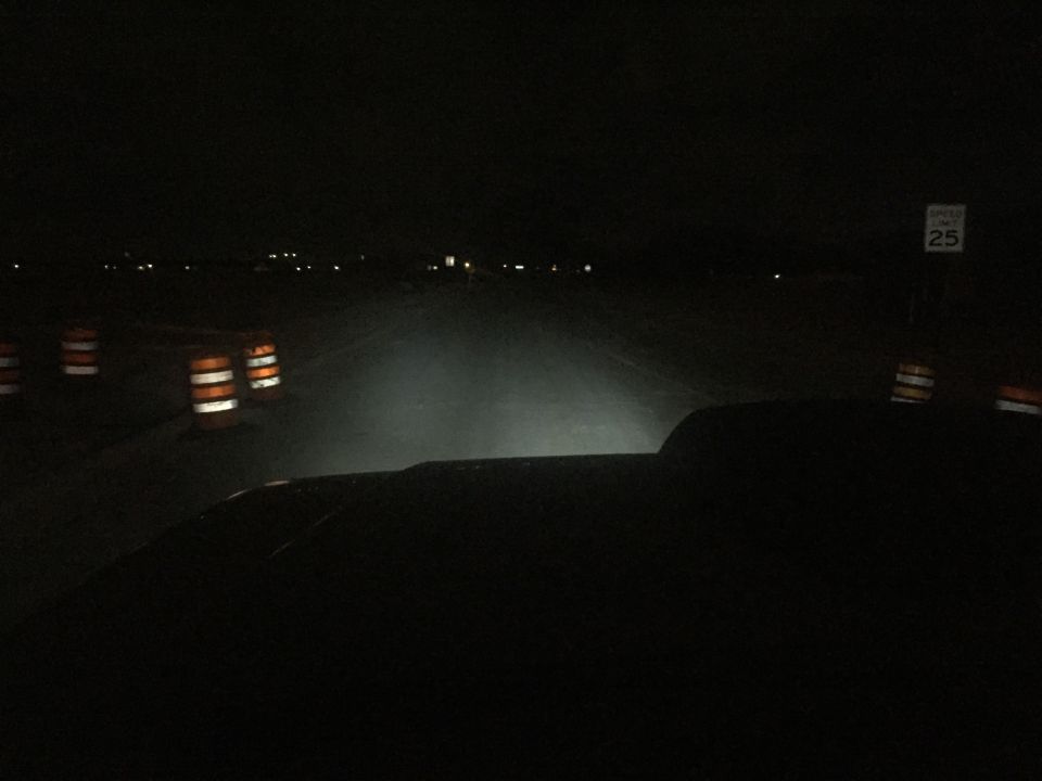 view from inside a vehicle at night, headlights on, with traffic cones and a speed limit sign visible