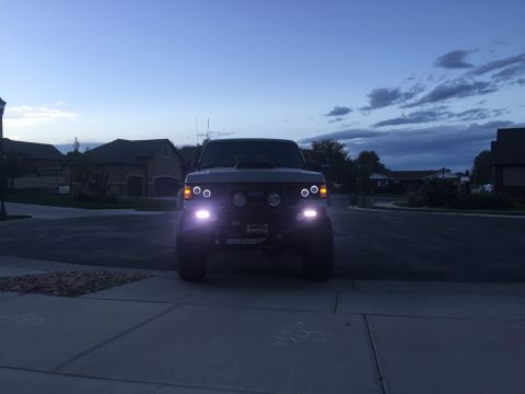 1988 Ford Bronco - A dark gray Ford Bronco is parked in a driveway at dusk, its headlights illuminated.