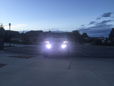 1988 Ford Bronco - A truck sits in a driveway at dusk with its headlights illuminated, casting a bright glow.