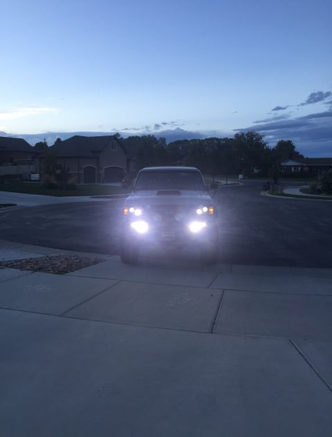 1988 Ford Bronco - An SUV sits in a driveway at dusk, its headlights illuminating the twilight sky.