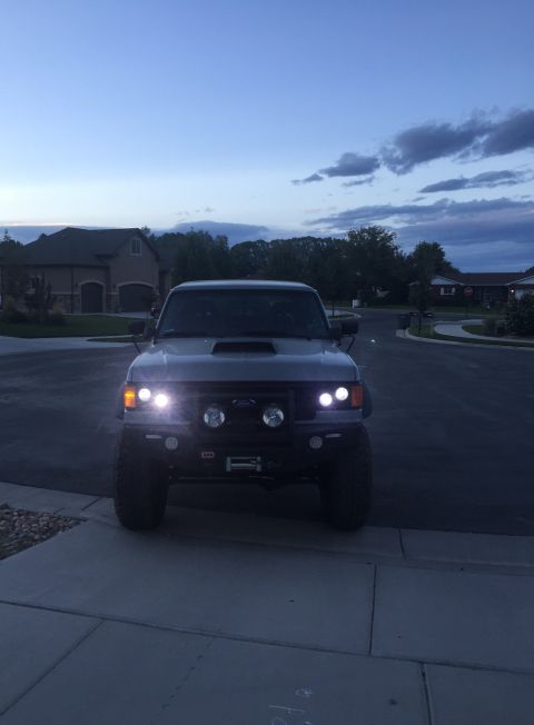 1988 Ford Bronco - A gray 1988 Ford Bronco is parked in a driveway at dusk, its headlights illuminated.