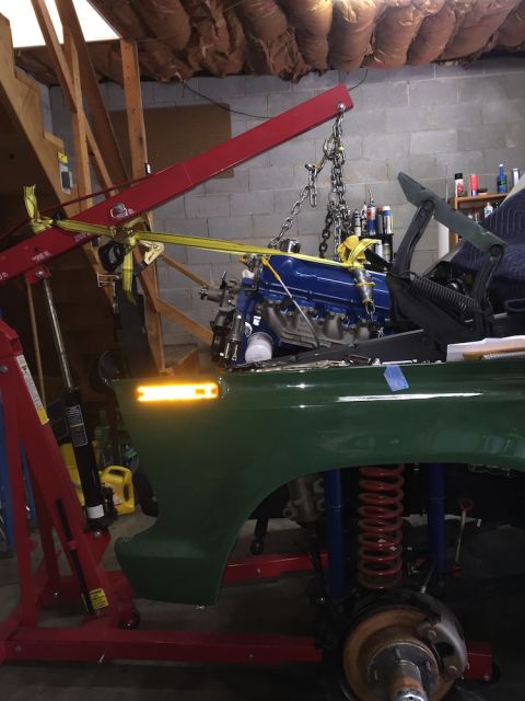 1978 Ford Bronco - An engine is being lowered into a green vehicle using an engine hoist. The vehicle's front end and suspension are exposed.