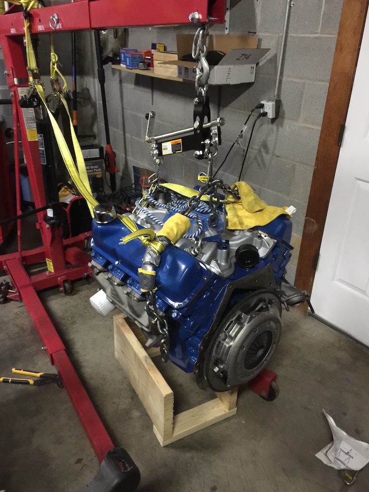 Blue engine with clutch assembly, suspended by engine hoist and straps
