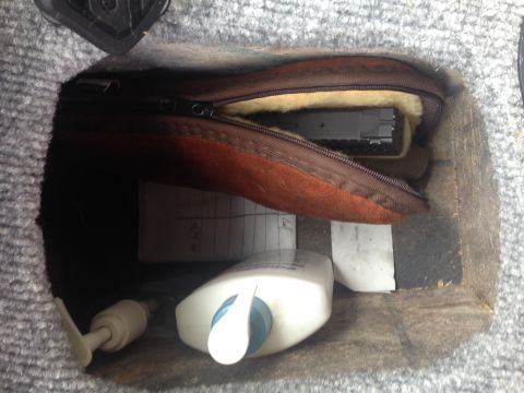 2001 Ford Ranger - A firearm is stored in a zippered pouch alongside a lotion bottle and some documents within a vehicle's storage compartment.