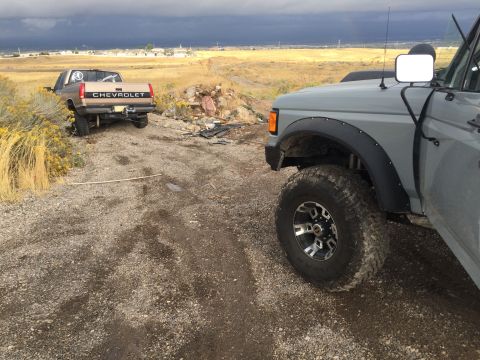 1988 Ford Bronco - A gray SUV, likely from 1988, is parked on a dirt road next to a tan Chevrolet pickup truck.