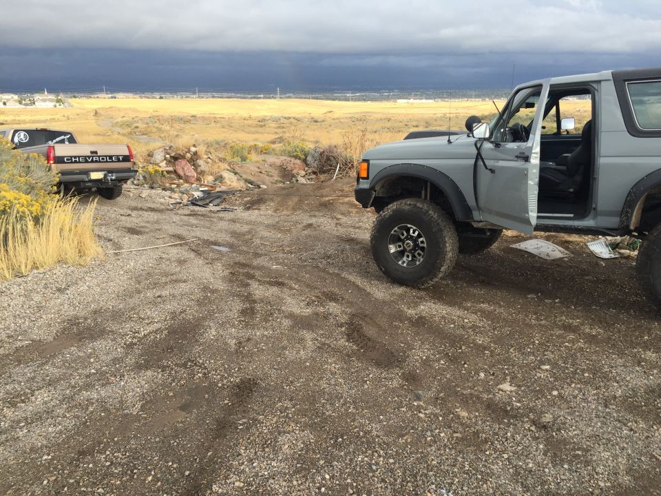 1988 Ford Bronco with driver door open, parked next to a Chevrolet pickup truck in a dry, open area