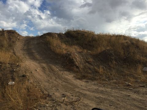 1988 Ford Bronco - A dirt track winds up a dry, grassy hill under a dramatic sky.